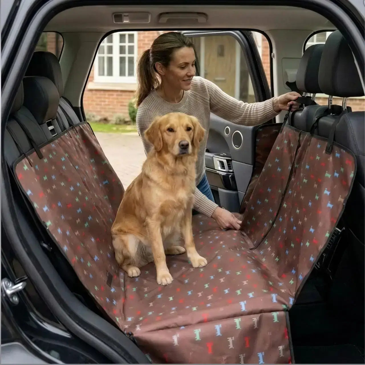 Une femme avec son golden retriever assis sur une housse de protection pour chien pour voiture marron au motif de chien.