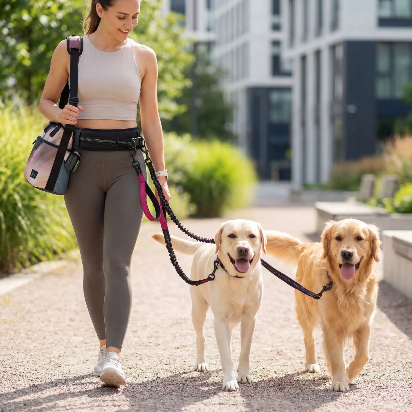 Une femme marche avec ses deux chiens avec la laisse pour chien main libre rose en ville.