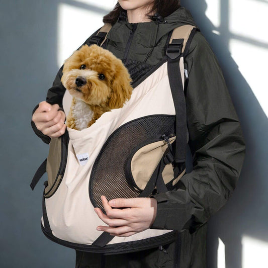 Une femme portant son sac à dos devant elle, accompagnée d'un caniche brun.