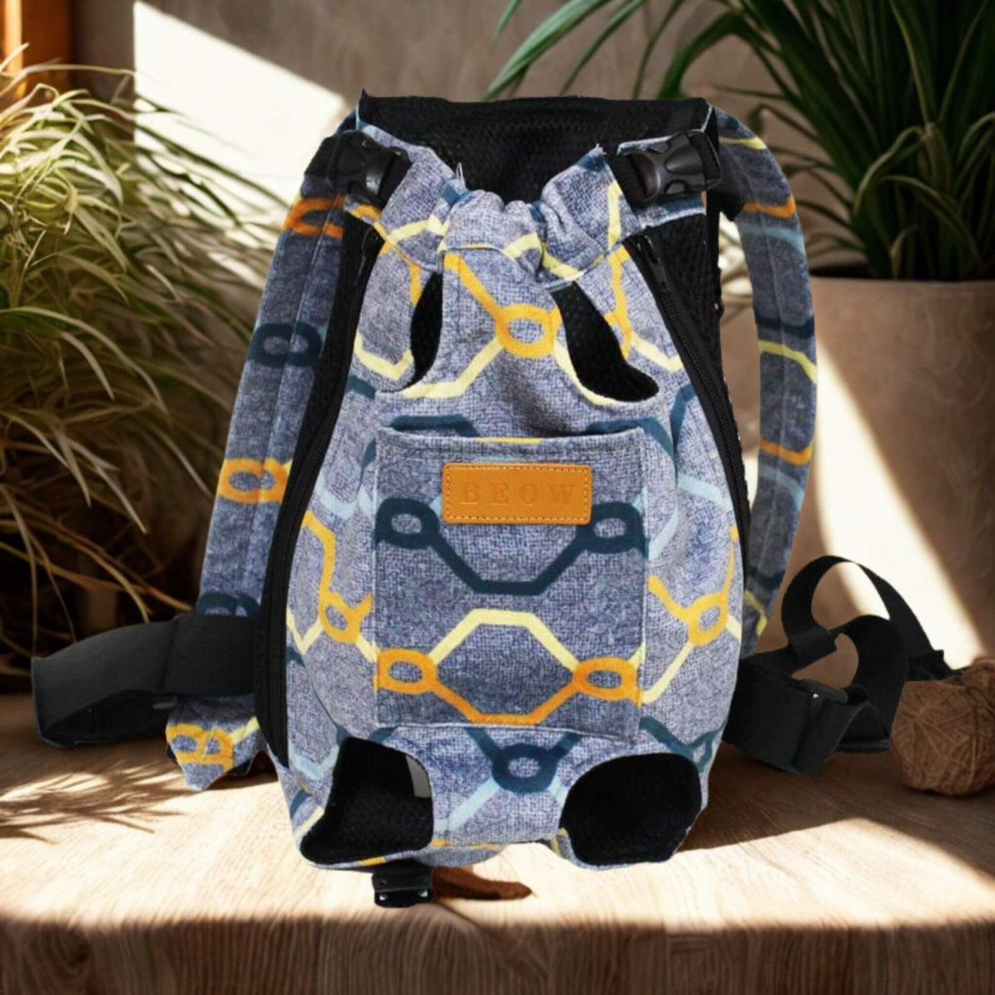 Un sac à dos pour chien porté par l'humain de couleur bleu avec rayures colorées sur une table avec plante à côté.
