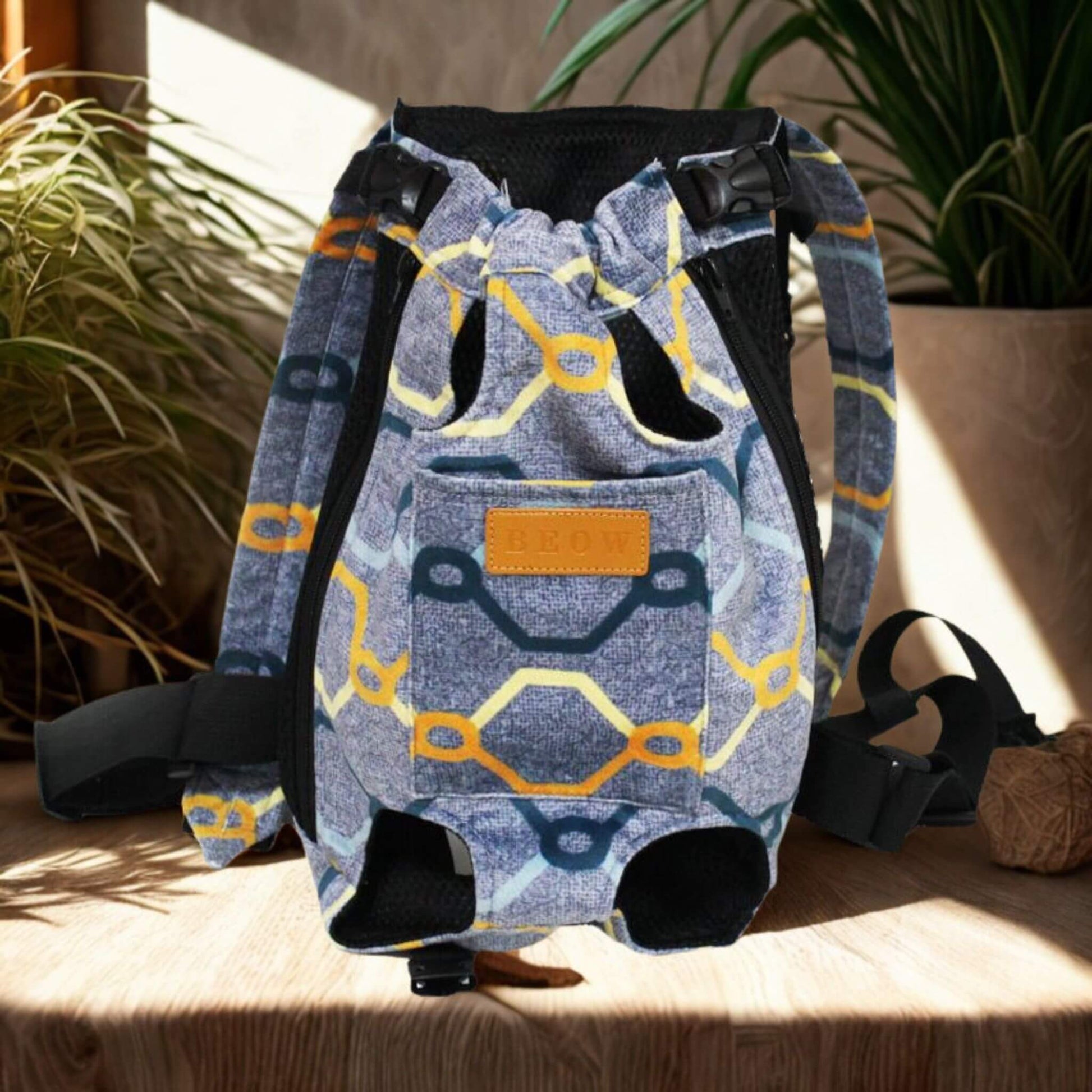 Un sac à dos pour chien porté par l'humain de couleur bleu avec rayures colorées sur une table avec plante à côté.
