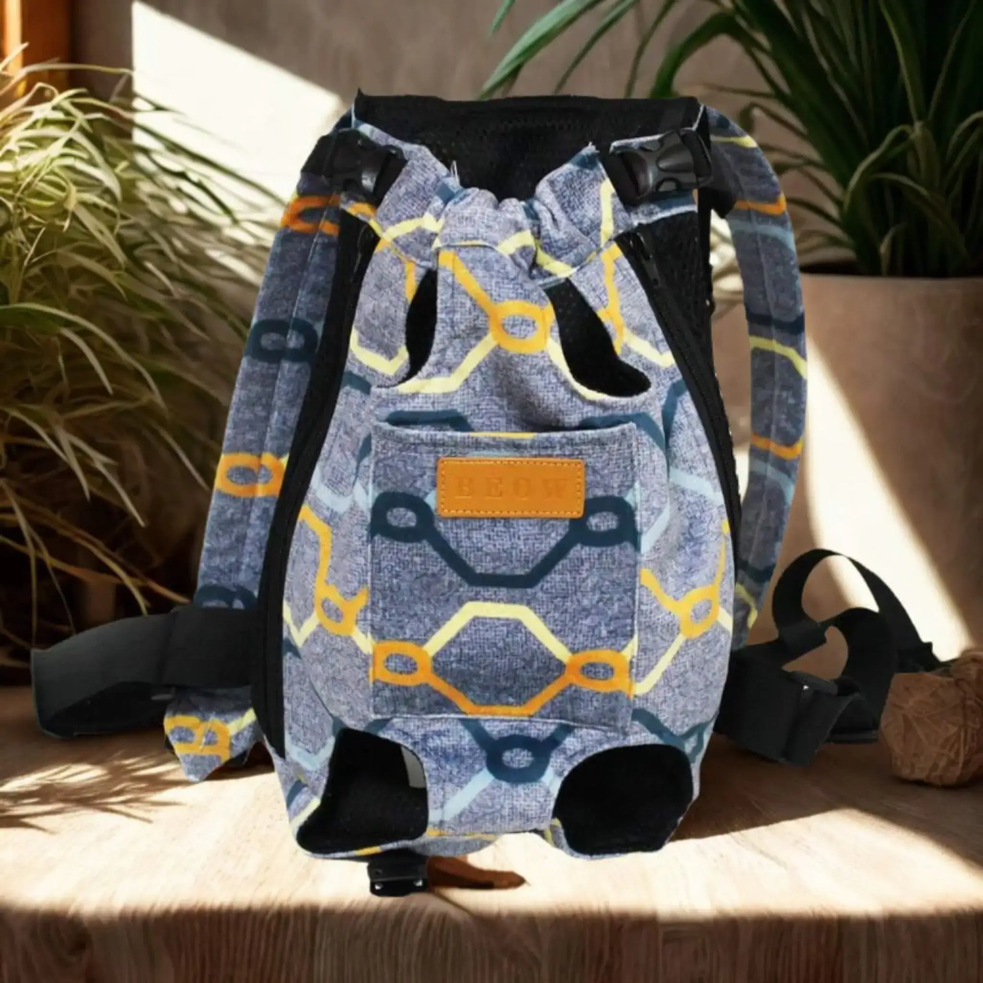 Un sac à dos pour chien porté par l'humain de couleur bleu avec rayures colorées sur une table avec plante à côté.