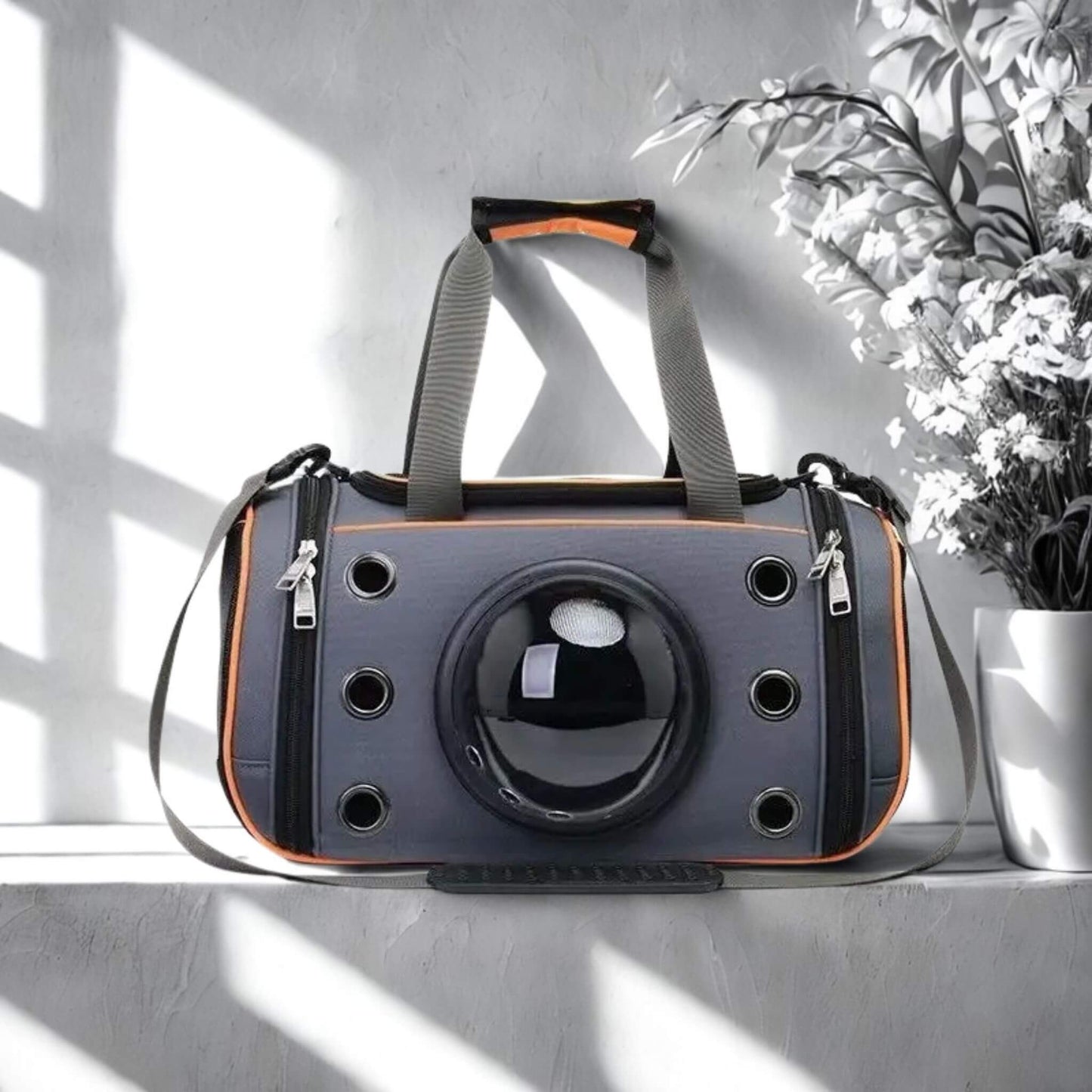 Un sac à dos pour chien de couleur gris et orange sur un rebord mural avec un vase de fleurs blanches à côté.