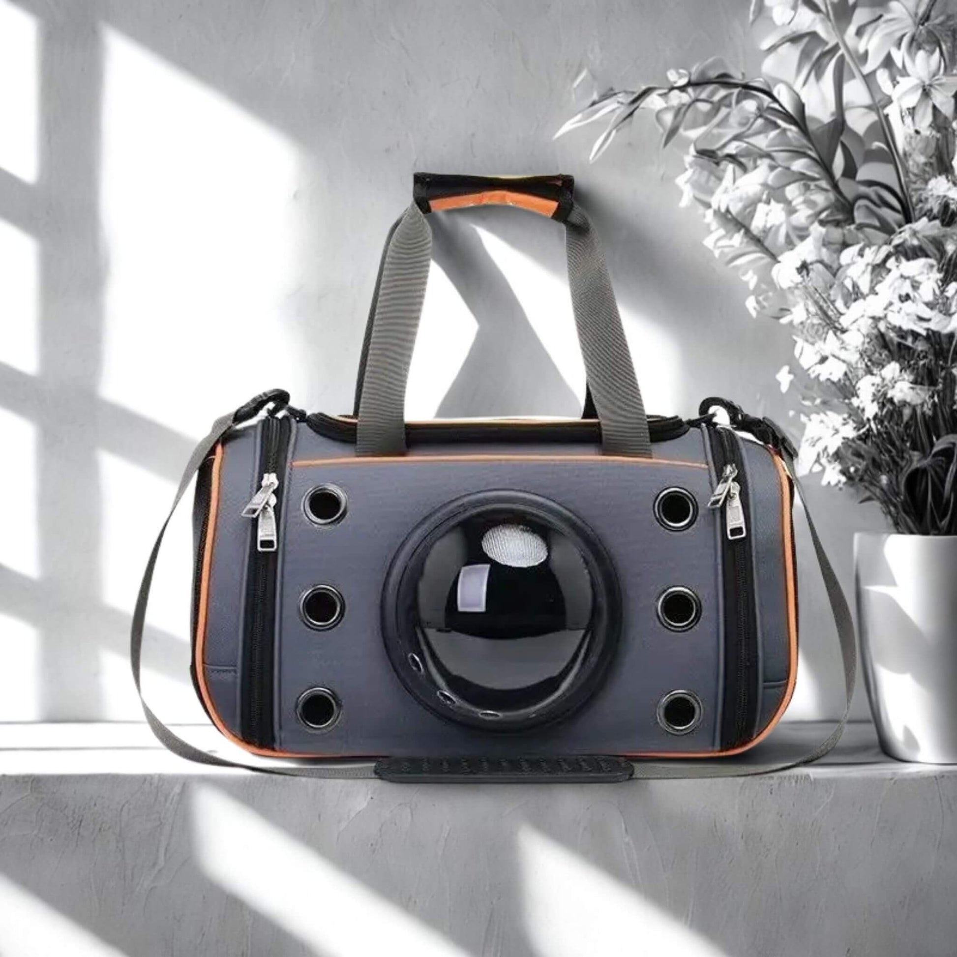 Un sac à dos pour chien de couleur gris et orange sur un rebord mural avec un vase de fleurs blanches à côté.