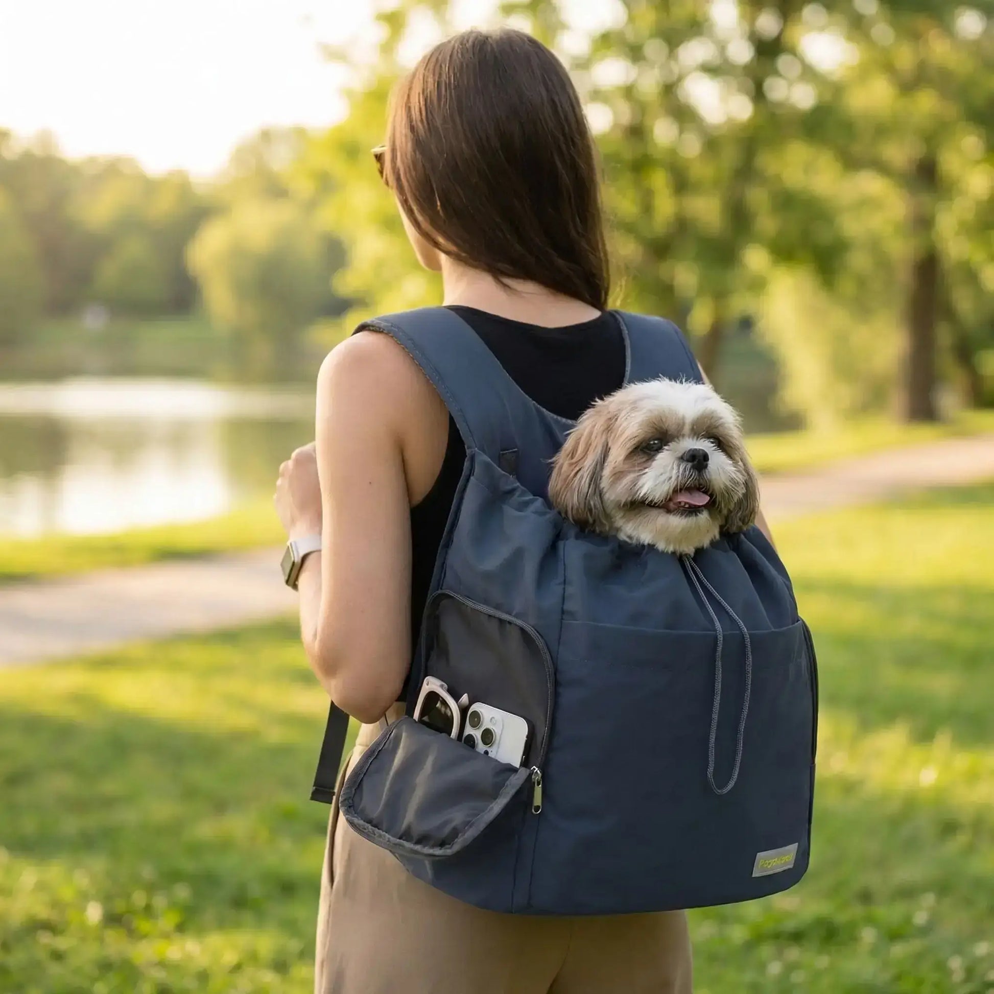 Une femme vue de dos transporte son shih tzu dans un sac à dos pour chien de randonnée.
