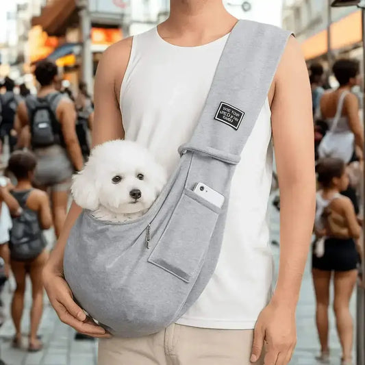 Un homme porte en bandoulière un sac pour chien gris avec son bichon frisé à l'intérieur dans une place public.