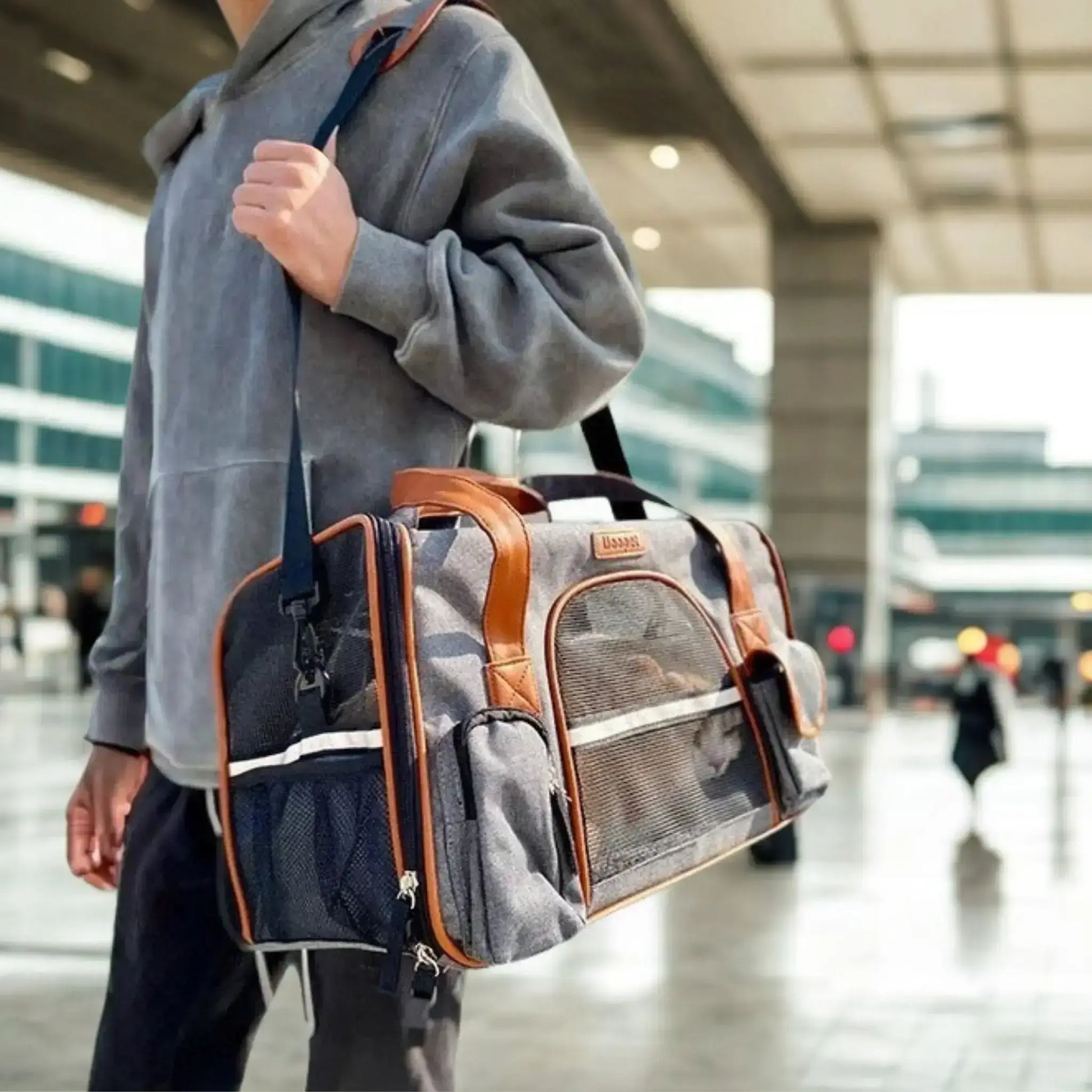 Un homme à l'aéroport porte sur l'épaule un sac de transport pour chien gris foncé.