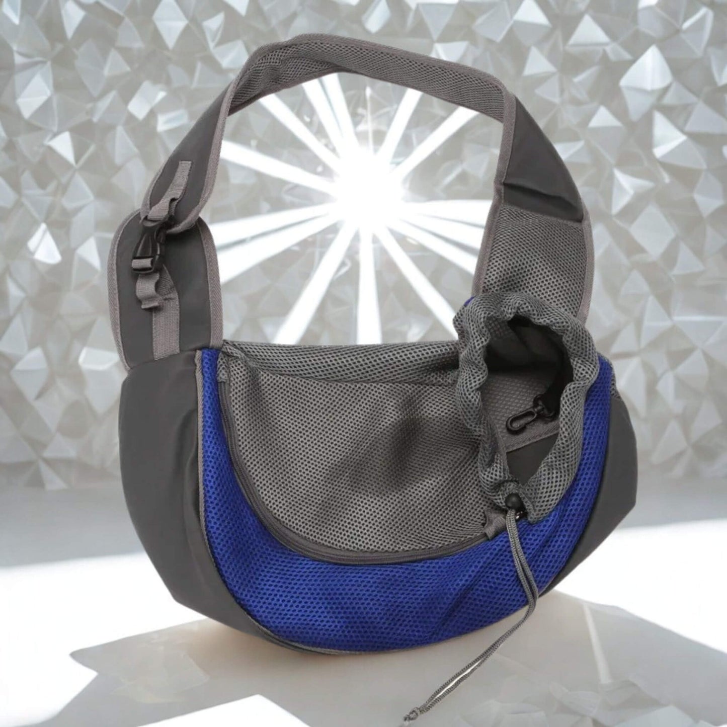 Un sac à bandoulière pour chien porté par un humain gris et bleu sur une surface blanche brillante