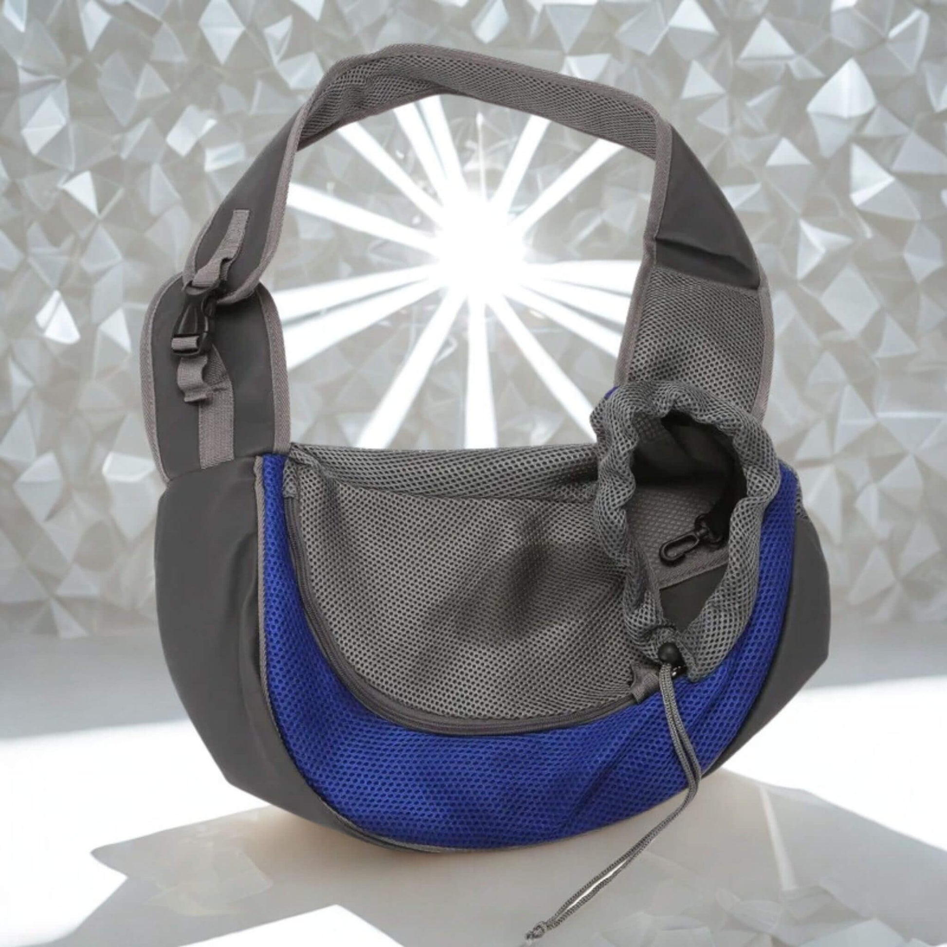 Un sac à bandoulière pour chien porté par un humain gris et bleu sur une surface blanche brillante