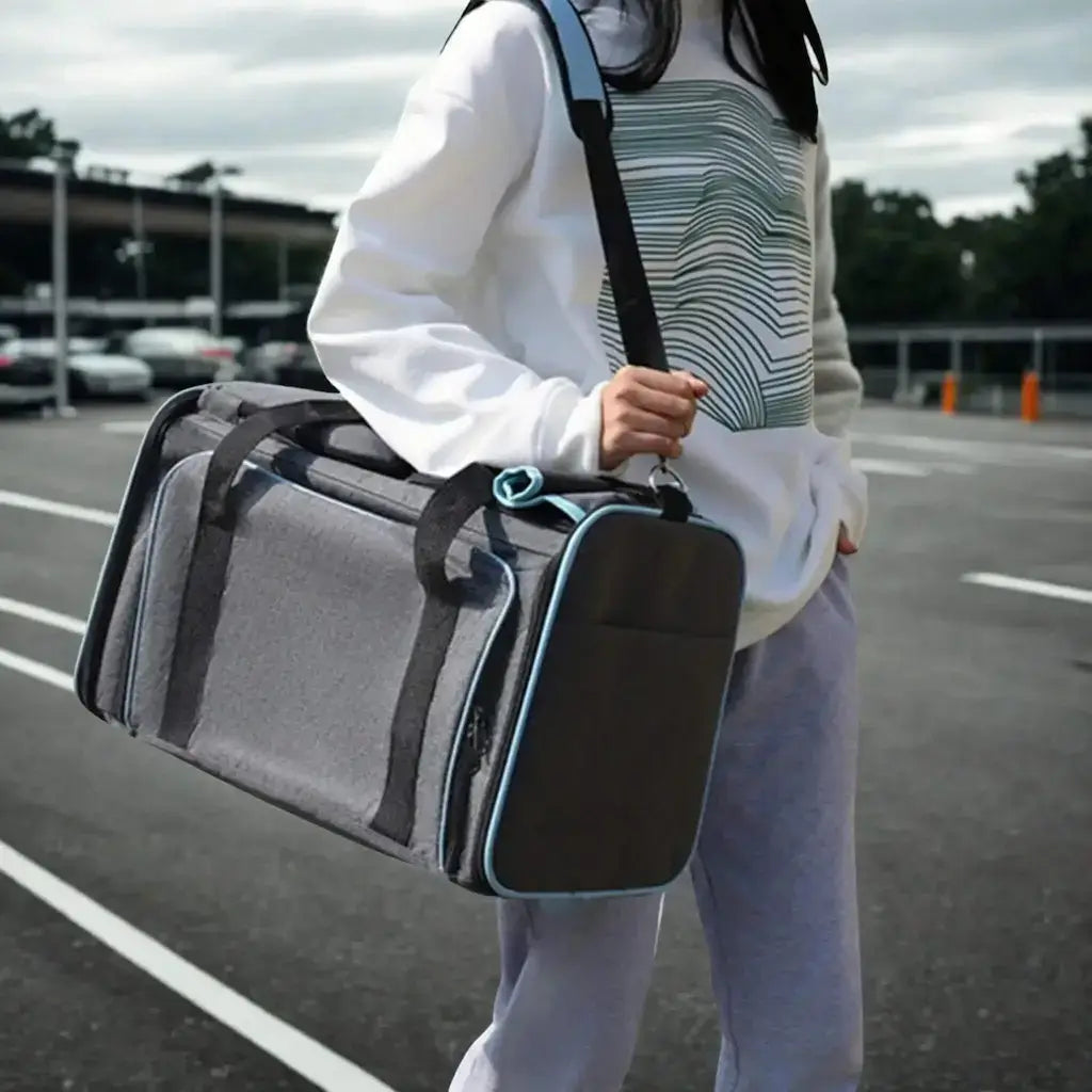 Une femme porte à l'épaule le sac de transport pour chien gris et bleu dans un stationnement. 