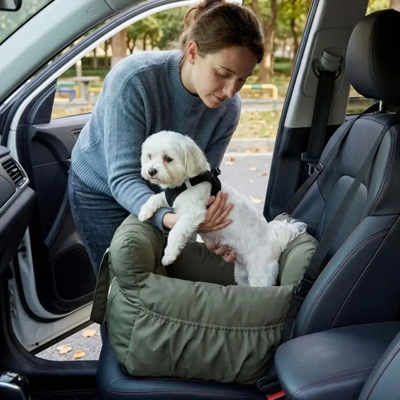 Une femme met en place son bichon frisé dans son siège d'auto pour chiens vert.