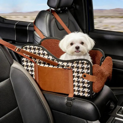 Un bichon maltais dans son siège d'auto pour chiens sur l'accoudoir de la voiture.