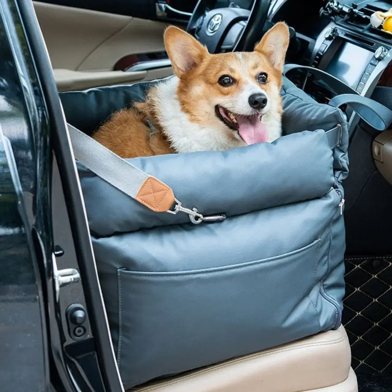 Un corgi assis dans son siège d'auto pour chien bleu sur le siège avant de la voiture.