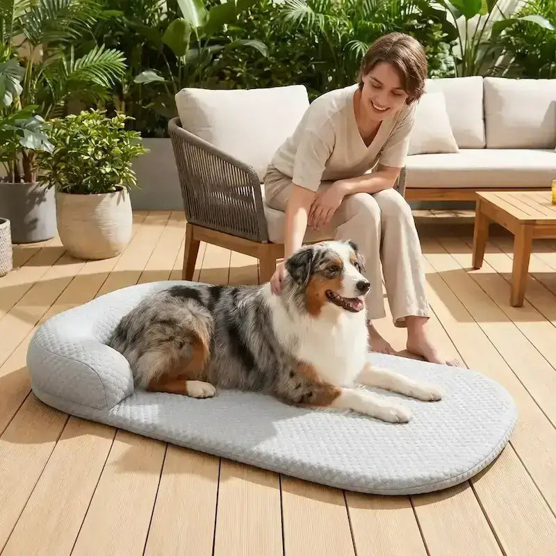 Une femme sur une terrasse caresse son berger australien allongé sur un tapis rafraichissant pour chien.
